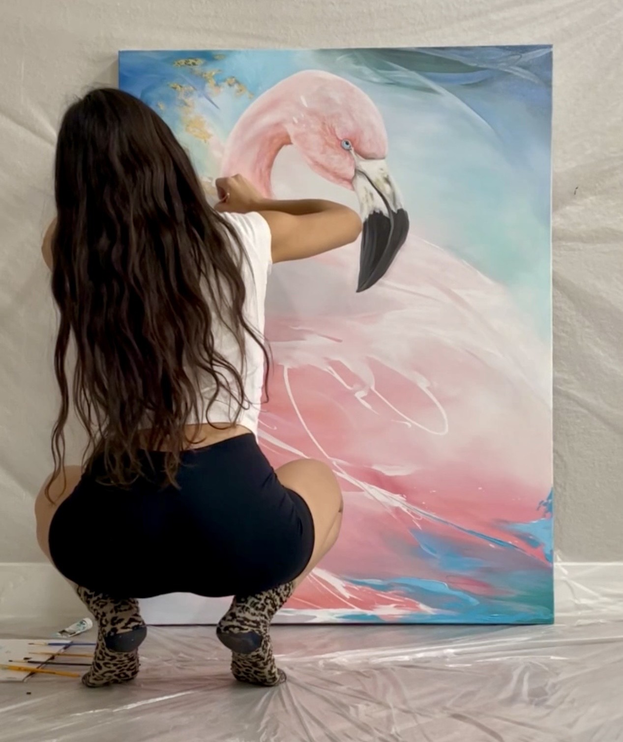 Karin Rave painting Cotton Candy — crouched before a large canvas of a pink flamingo in blue and rose